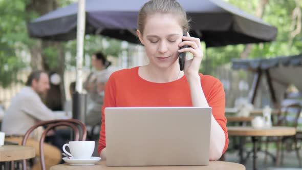 Young Woman Talking on Phone While Sitting in Cafe Terrace alt