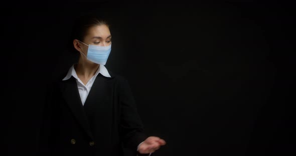Woman in a Medical Mask Points with Her Palm to an Empty Copy Space on the Right