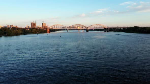 Establishing Aerial View Shot of Summer Down Kyiv Cityscape with Railway Bridge Over the River alt