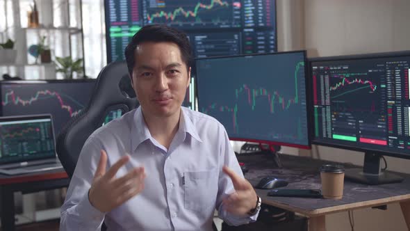 Asian Male Stock Market Broker Speech To Camera With Analyzing Graphs On Multiple Computer Screens alt