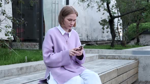 Lady Blonde with Short Hair Types on Black Phone in Street