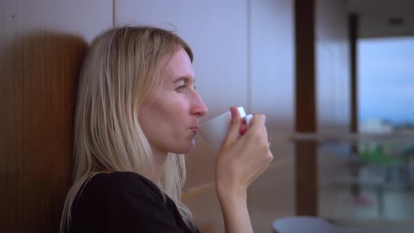 Young and beautiful woman with cup of hot coffee looks out window alt