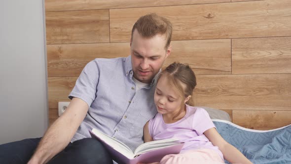 Handsome Young Father Explaining Paragraph Presented in Textbook to His Little Daughter