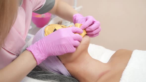 Collagen face mask. Beautiful young girl receiving facial cleansing procedure at a cosmetologist. alt