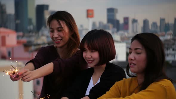 Happy group of asia girl friends enjoy and play sparkler at roof top party at evening sunset. alt
