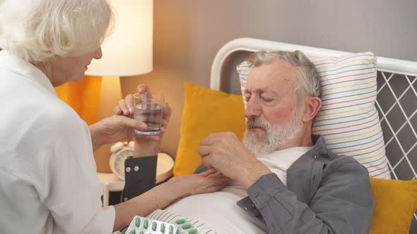 Aged Female Concerned with Health Condition of Husband Checking Fever Temperature Lying on Bed alt