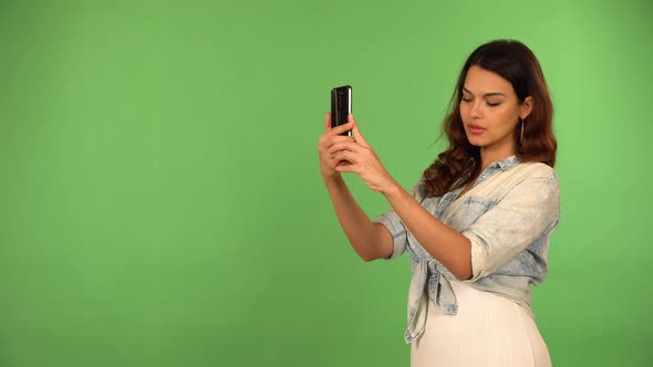 A Young Beautiful Caucasian Woman Takes Selfies with a Smartphone  Green Screen Background