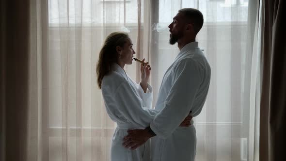 Lovers are Smoking Ecigarette in Hotel Room Man and Woman are Wearing White Robes alt