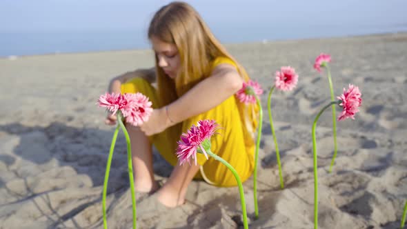Girl Sitting with Flowers Planted in the Sand of the Beach alt