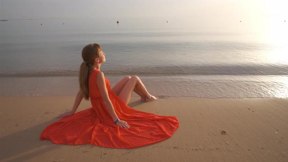 Young Happy Woman Wearing Red Dress Resting on Sea Beach Enjoying Warm Summer Morning alt