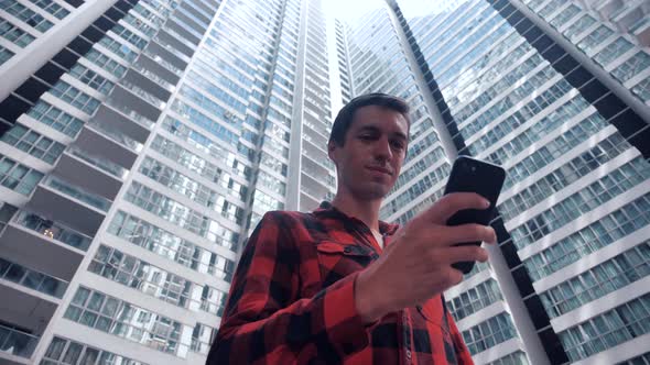 Portrait of Young Man in Plaid Shirt Browsing His Smartphone in City alt