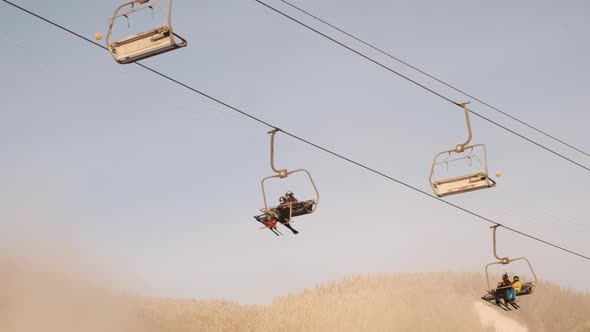 Skiers on Chair Lift Move Climb Up on Sunny Winter Morning Backdrop of Blue Sky Pine Forest in Snow alt