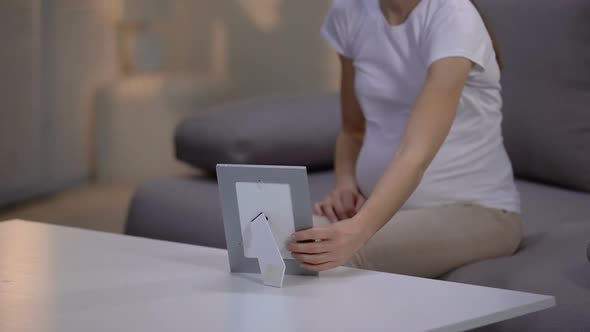 Young Unhappy Pregnant Widow Looking at Photo in Frame, Suffering Loneliness alt
