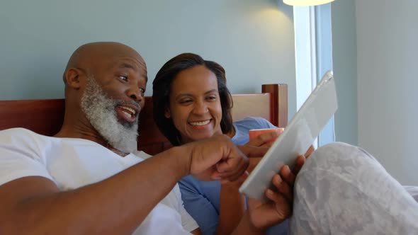 Front view of mature Caucasian couple using digital tablet on bed in a comfortable home 4k alt