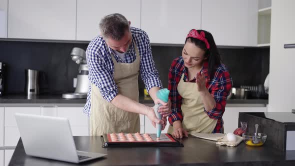 Man Piping Out Macaron Mixture on a Slip Mat with Wife's Support alt