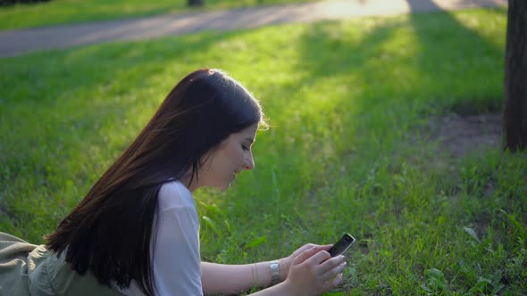 Attractive Woman Lies on Grass in Park Use Smartphone Relaxing Summer Holidays