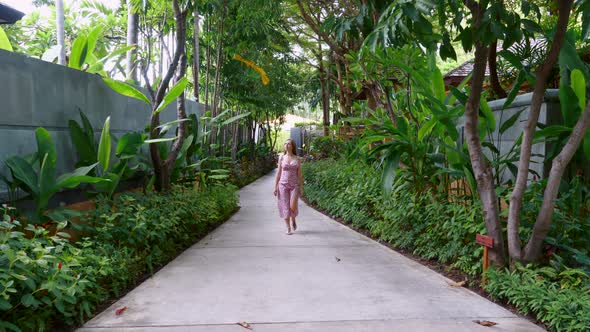 Young Beautiful Woman Walking Among Green Tropical Trees at a Luxury Hotel Area alt