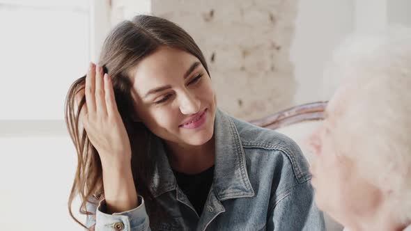 Cheerful Young Girl Talking with Senior Woman on Sofa in Light Room alt