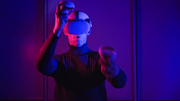 Young Man Plays a Game in Virtual Reality Using VR Headset and Controllers alt