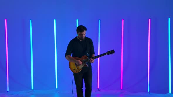 Musician Playing on Electric Guitar Against the Background of Multicolored Neon Lamps in the Studio alt
