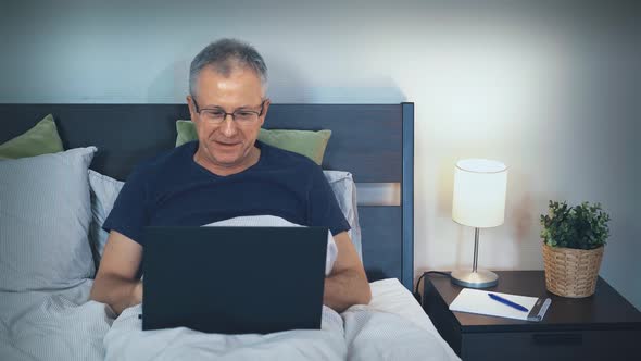 A Middleaged Man Communicates Via Video Link with Relatives and Friends on a Computer Lying in Bed