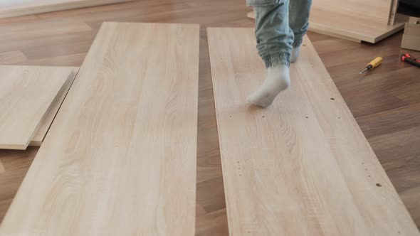 Child in Cargo Pants and Gray Socks Runs Over Pieces of Chipboard on Floor alt