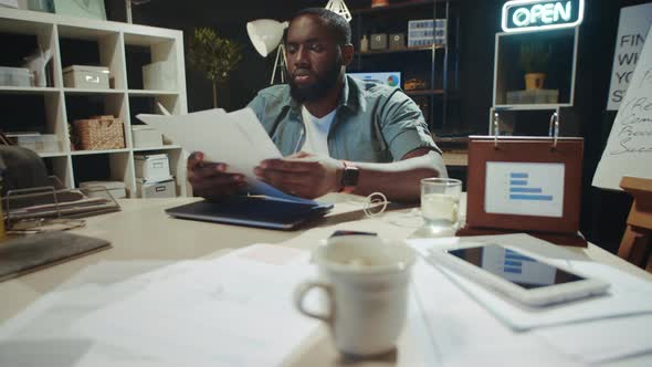 Focused African American Businessman Reading Business Report in Late Office. alt