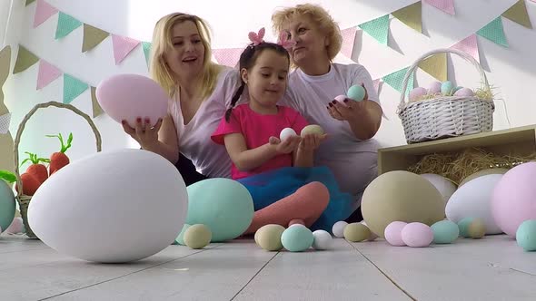 Little Girl Sharing Decorated Eggs with Mother and Grandmother at Easter Dinner with Family
