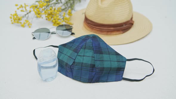 Flat lay of coronavirus travel kit: fashion mask, hand sanitizer, sunglasses and hat alt