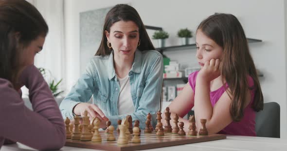Young mother teaching chess to her daughters