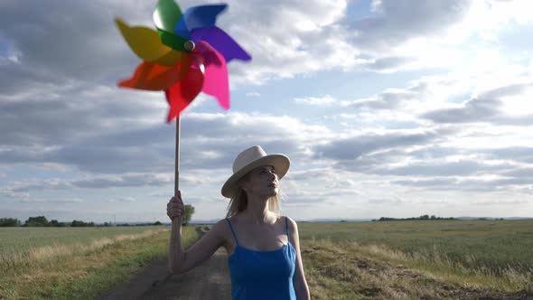 Girl in hat and blue dress with pinwheel on rural road