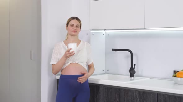 Pregnant Woman Stands in the Kitchen and Drinks Water From a Glass