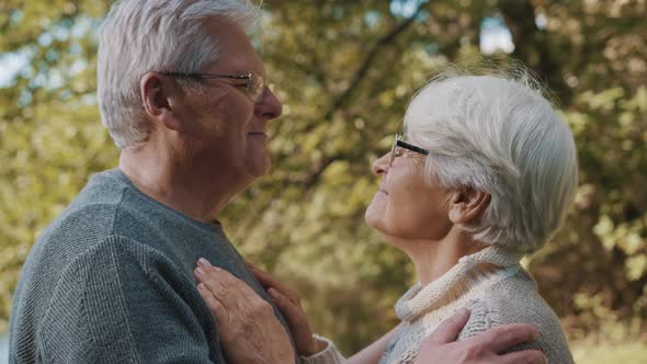 Happy Old Couple Dancing at Autumn Park. Senior Man Flirting with Elderly Woman. Kiss in Forehead in alt