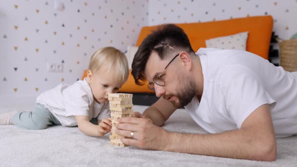 Dad and Toddler Son Playing Together and Building a Wooden Blocks Tower at Home alt