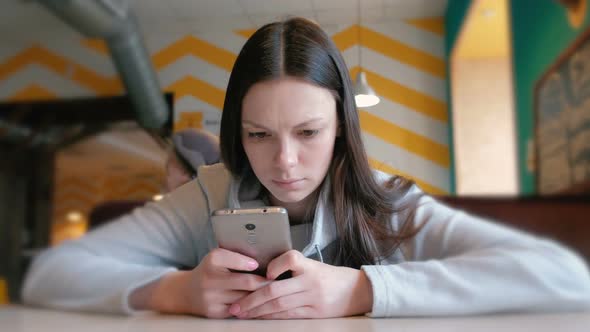 Young Seriously Woman Reading Something on Her Mobile Phone Sitting in Cafe