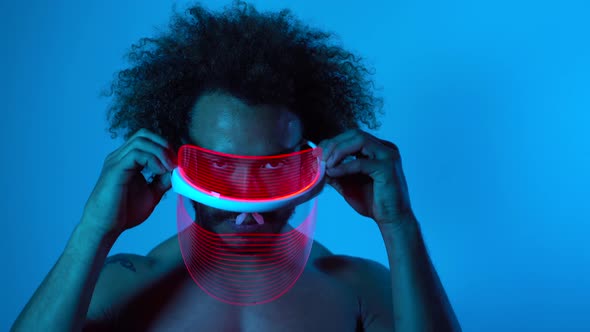 Man wearing light therapy mask against blue wall alt