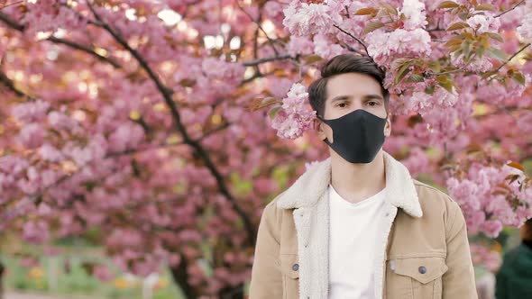 Pandemic, portrait of a young man on a woolen jacket on black virus protective mask on street.  alt