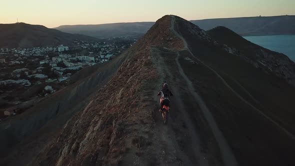 Drone View of Man on Motorbike Extremely Rides Across the Hills with Black Sea on Background 