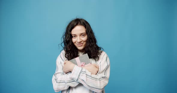 A Young Girl Receives a Gift in a Beautifully Packaged Box on a Blue Background alt