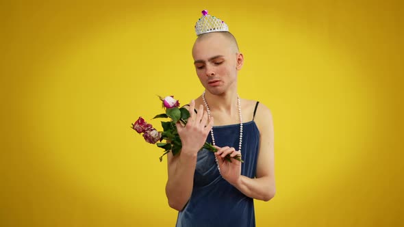 Young Sad Queer Man in Dress and Tiara Holding Bouquet of Withered Flowers Looking at Camera alt