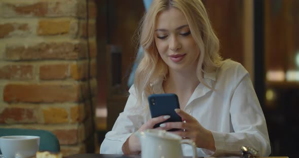 Attractive Woman Using Smartphone Drinking Coffee in Cafe alt