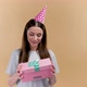 Happy Young Cheerful Birthday Girl with a Present Wearing Party Head on a Beige Background - VideoHive Item for Sale