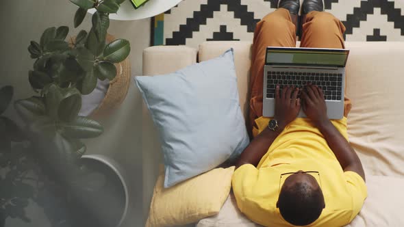 Afro-American Man Sitting on Sofa and Typing on Laptop alt