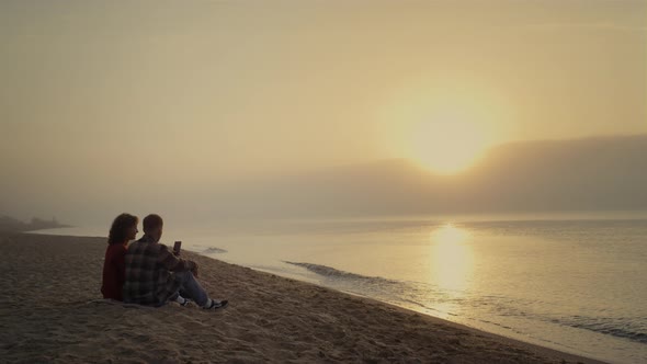 Couple Sitting on Beach at Sunset alt