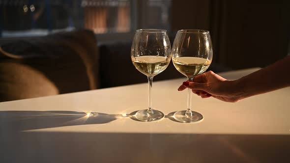 Female Hand Taking One of Two Glasses with Dry White Wine on White Table