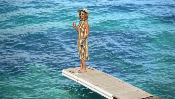 A woman with a glass of white wine on a dock over the Mediterranean Sea in Italy, Europe alt