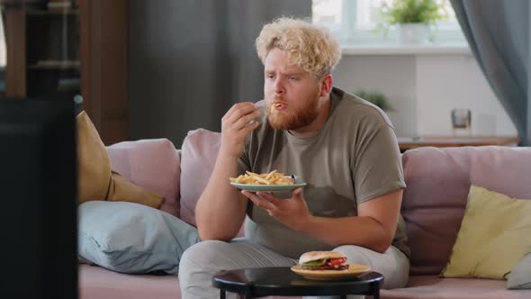 Obese Man Watching TV and Eating Fries at Home alt