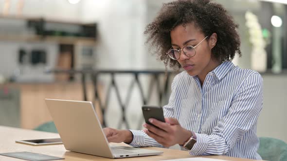 Hardworking African Businesswoman Using Smartphone and Laptop in Office  alt
