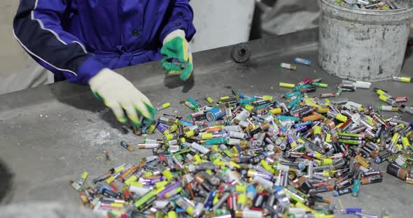 View of the Hands of a Person in Gloves Sorting Used Batteries