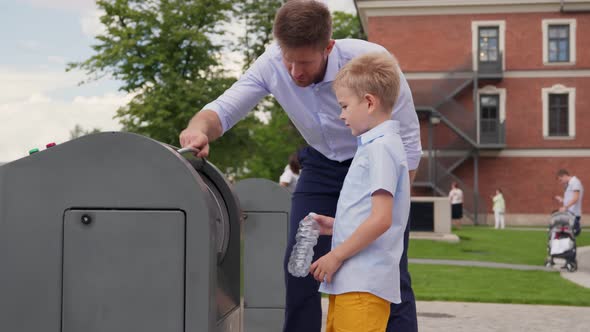 Father and Son Throwing Out Empty Bottle to Trash Bin Outdoors alt